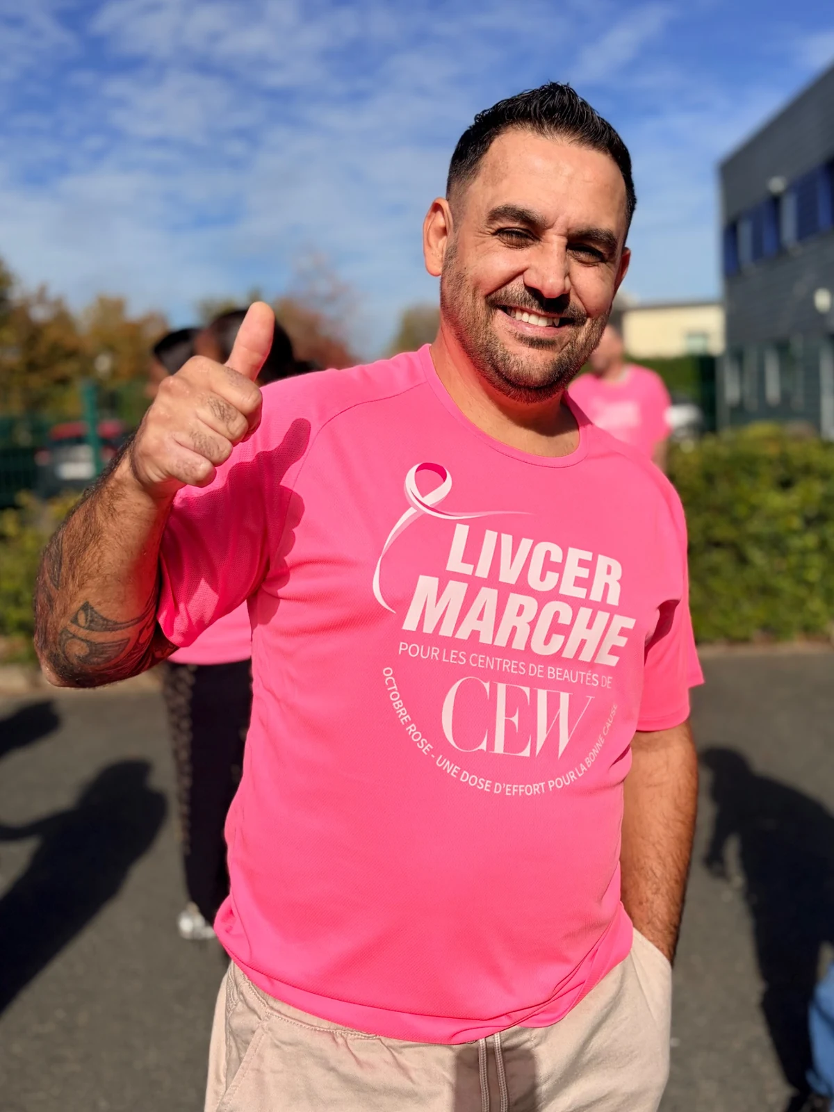 Un collaborateur en t-shirt rose adresse un signe enthousiaste à l’objectif.